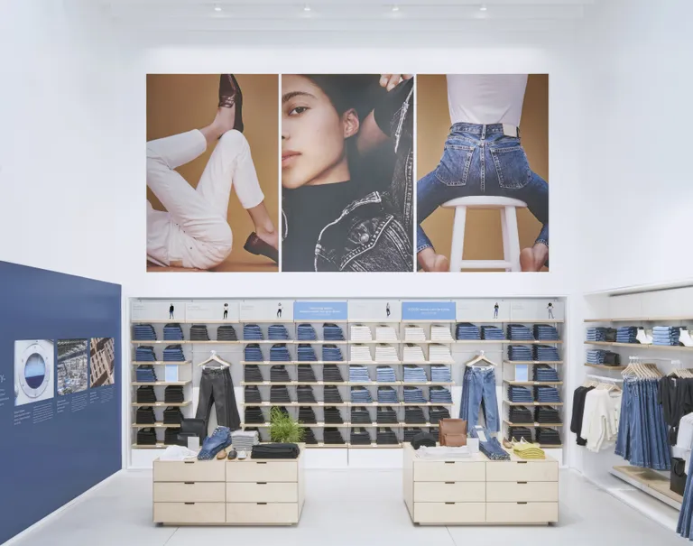 Series of images of a model posing in denim clothes are hung above wooden System 1224 shelves showcasing various neatly folded jeans. Wooden cabinets also displaying clothing articles stand in front of the shelves.