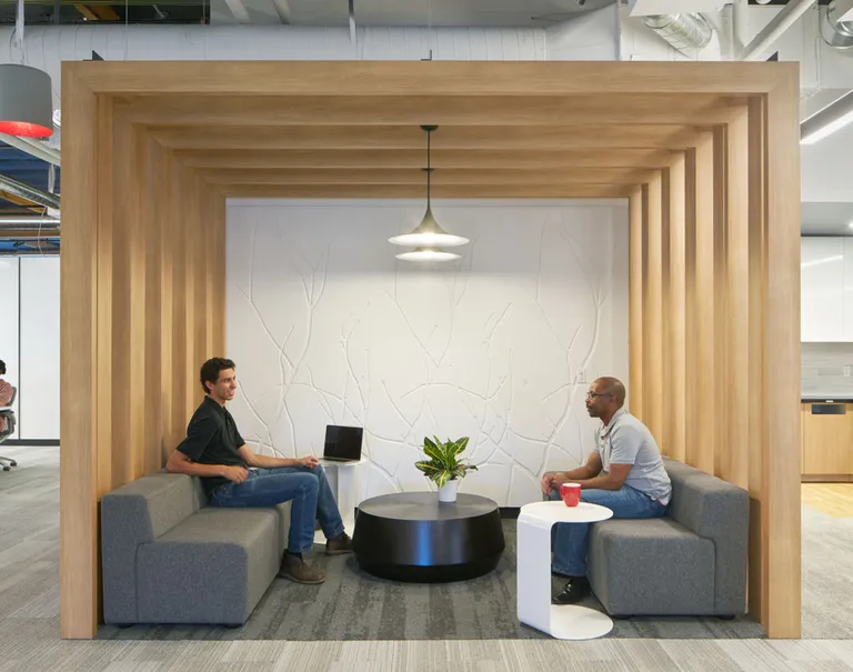 Two men sit in a lounge space divided off in a cubic shape by wooden Fortina panels. Within the cubic space is a white branch patterned Iconic Panel wall.