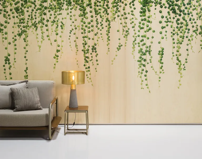 A gray couch and small wooden stand with lamp stand in the corner in front of a large wall decorated with Ivy plant patterned wooden Infused Veneer.