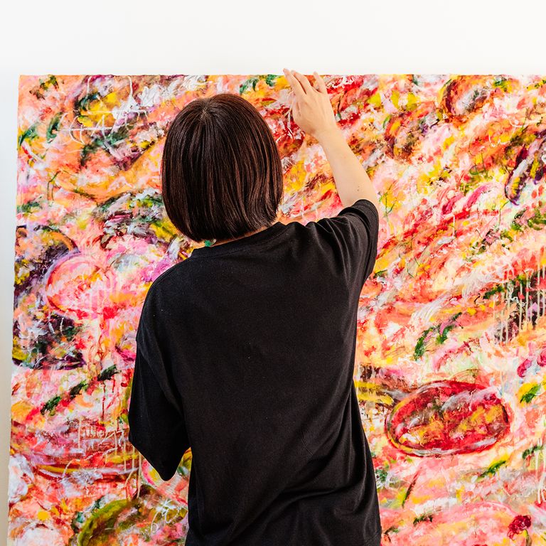 Ayako Rokkaku adding paint to the top of a colourful abstract canvas