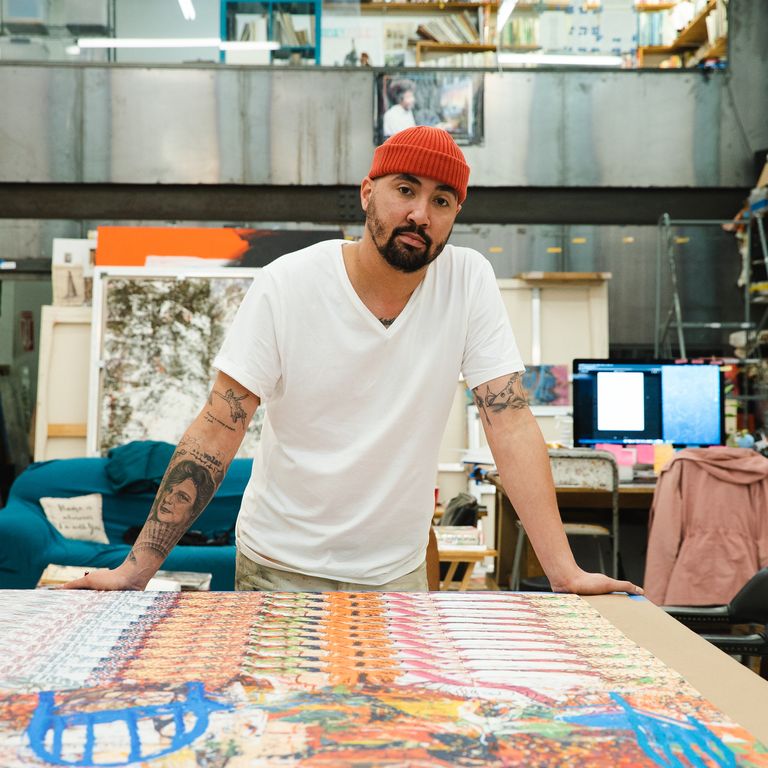 artist posing for a photo behind a table on which his prints are laid out – both of his hands are resting on the edge of the table