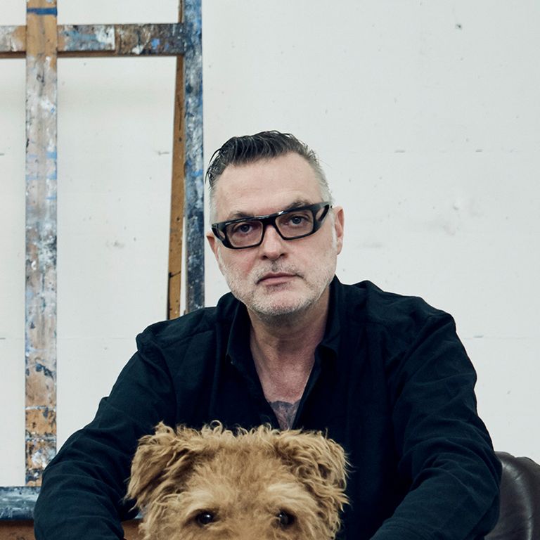 Artist sat in a black jacket with his dog looking directly to the camera
