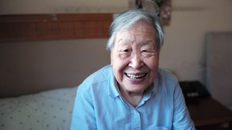 Dementia care- Photo of an asian older lady smiling at the camera wearing a blue shirt
