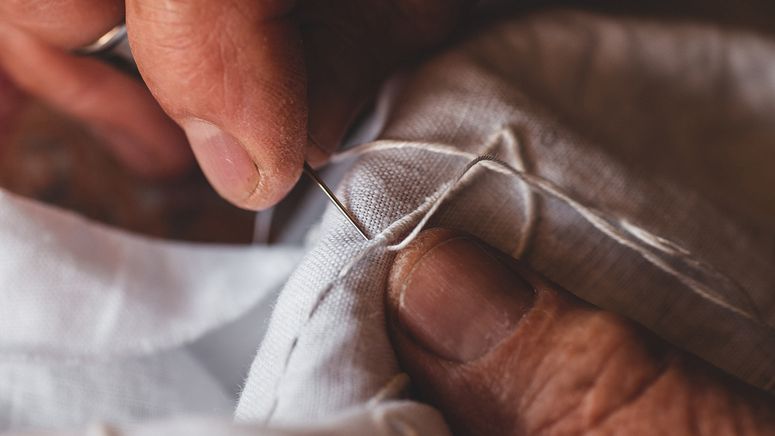 Close up photo of fingers sewing white cotton while caring for multiple people at once