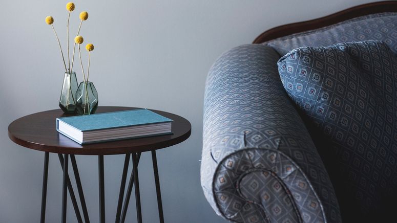 Photo of a veteran's room in residential aged care showing a blue lounge, round brown table with a blue book and yellow flowers in a vase on it