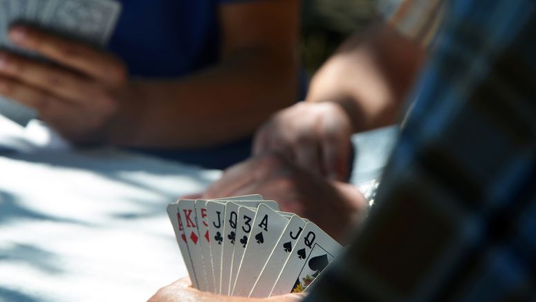 Aged care homes- cropped photo of three pairs of hands playing cards, the pair in the foreground are holding a mixed hand