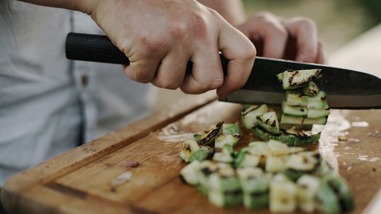 Aged care jobs- Cropped photo showing hands and knife chopping grilled zucchini