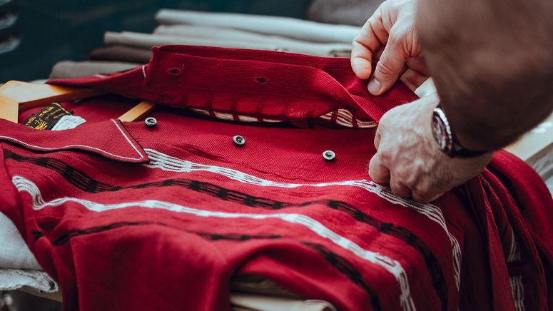 Home care package options- Close up photo of older hands buttoning a red shirt on a table