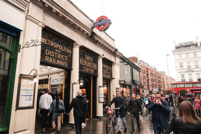 The exterior entrance of South Kensington underground tube railway station with a group of local people and tourism in the rainy season. 