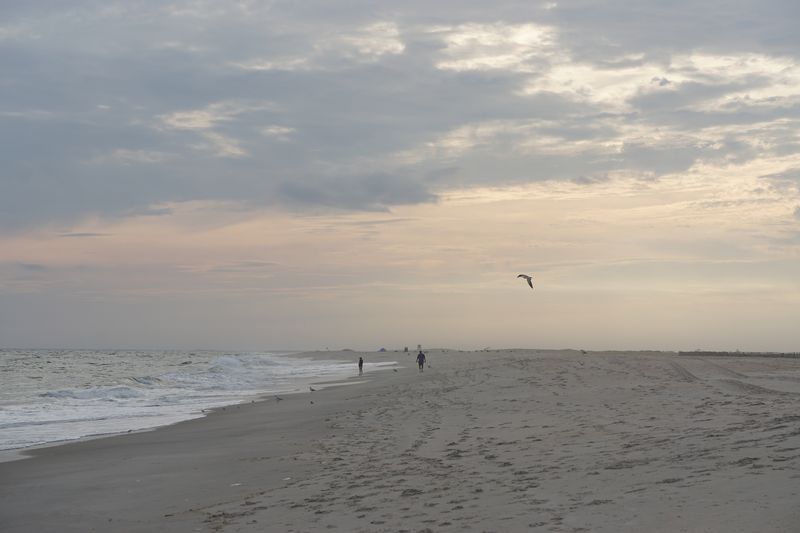 Jones Beach at sunset with some clouds and people walking on the beach in the distance