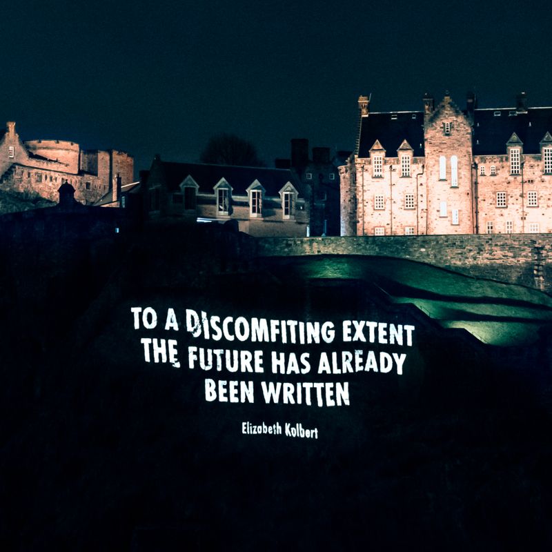 quote by Elizabeth Kolbert projected onto the cliff face below Edinburgh Castle, "To a discomfiting extent the future has already been written." 