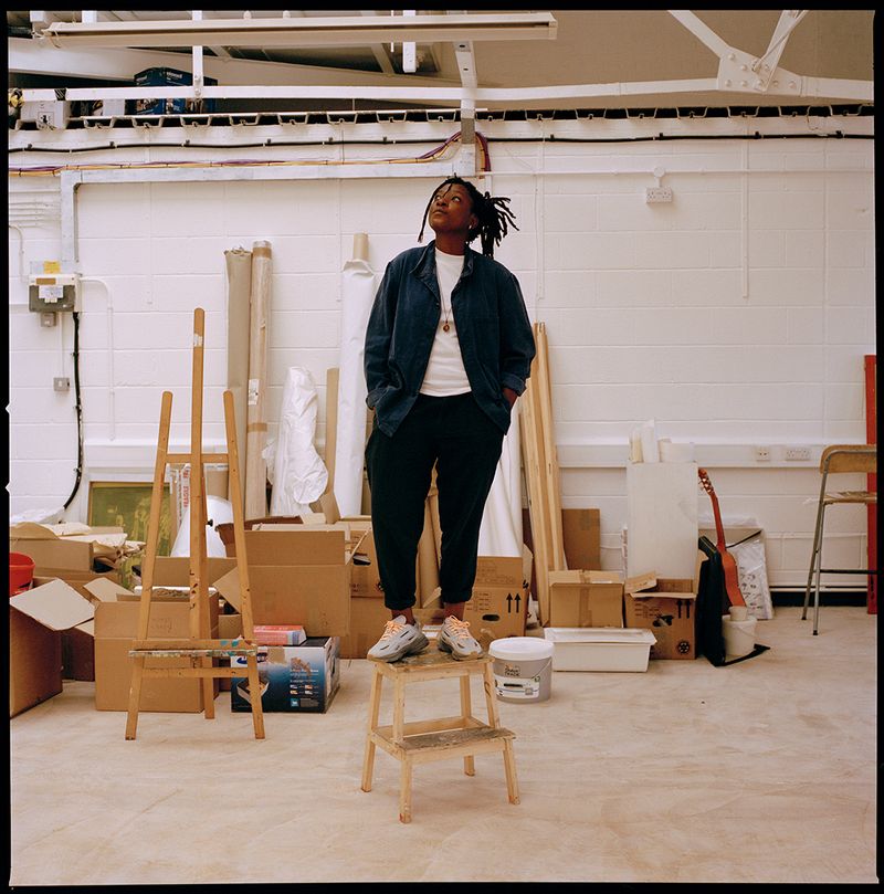 Kudzanai-Violet Hwami standing on a small step ladder in her studio