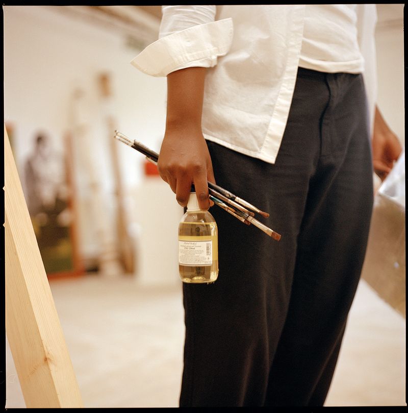 artist holding some brushes and a bottle of paint thinner