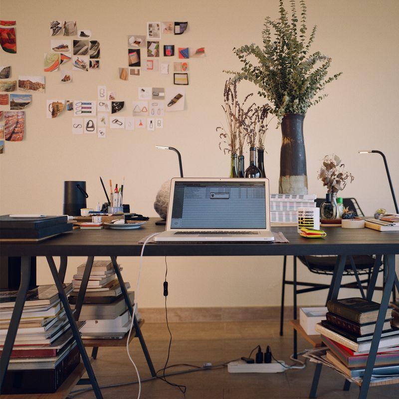 large desk with a macbook and large vase of eucalpyptus