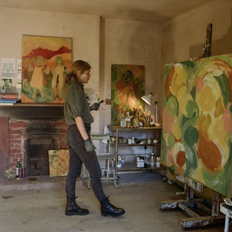 Antonia Showering inspecting a green and orange painting in her studio
