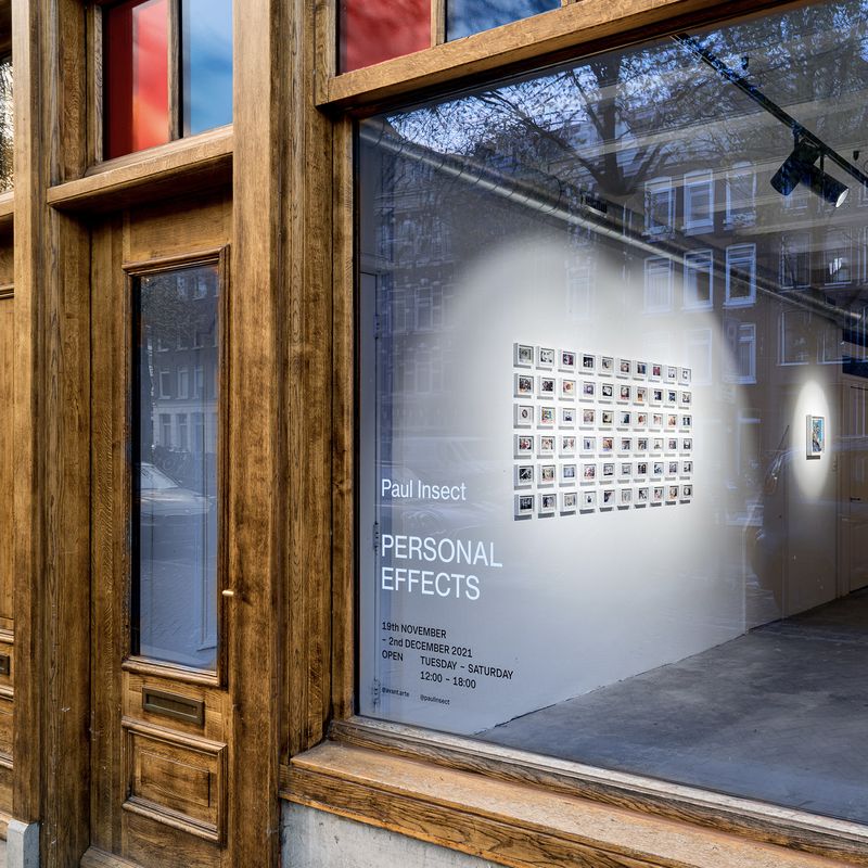 wooden building facade with large window, a grid of polaroids are visible on the wall inside
