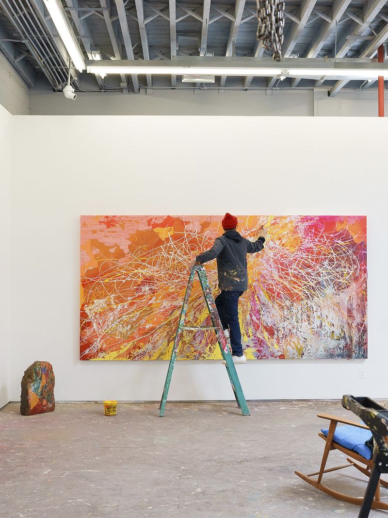 José Parlá painting a large abstract canvas on a step ladder