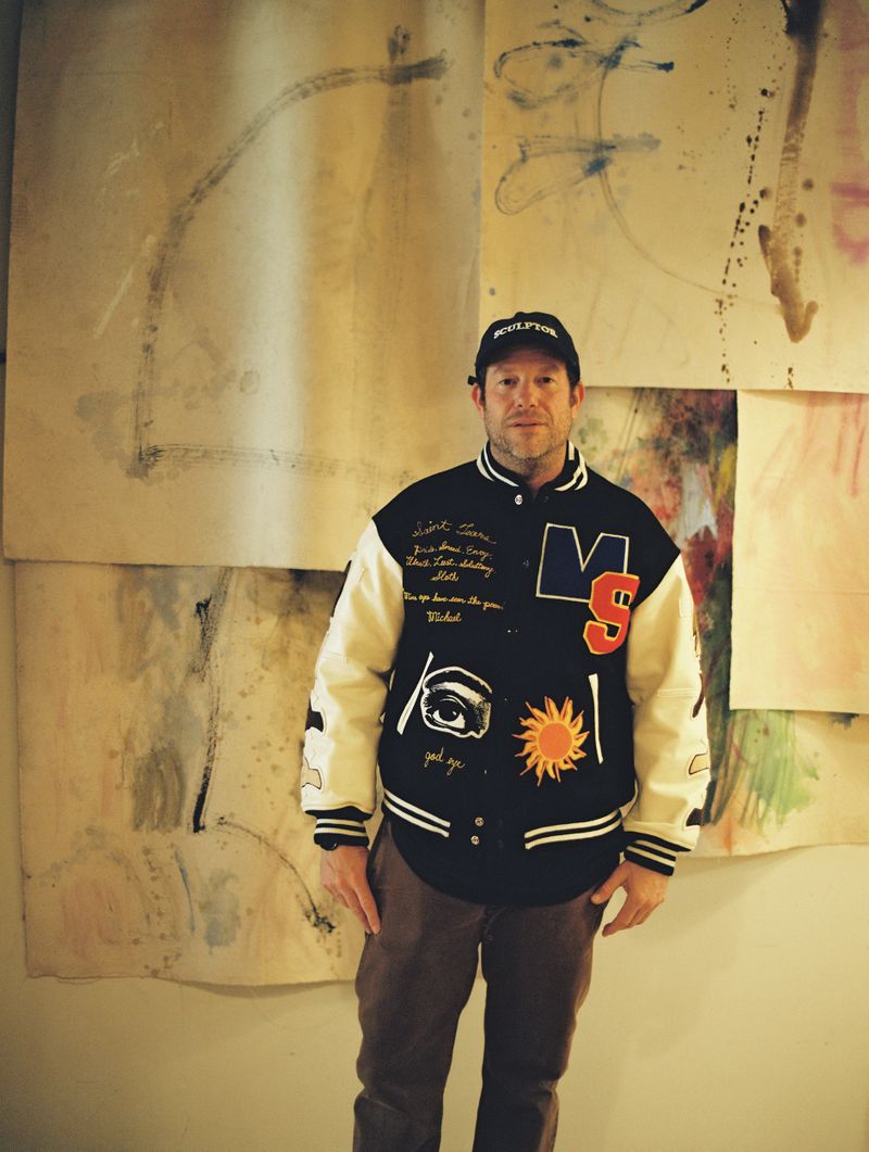 A man named Darren Romanelli is standing against a wall with multiple artworks