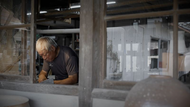 an old man leaning in a window of a ceramic studio