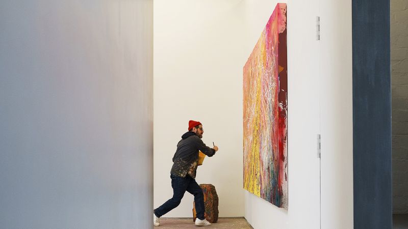 José Parlá striding towards a large abstract canvas, brush in hand