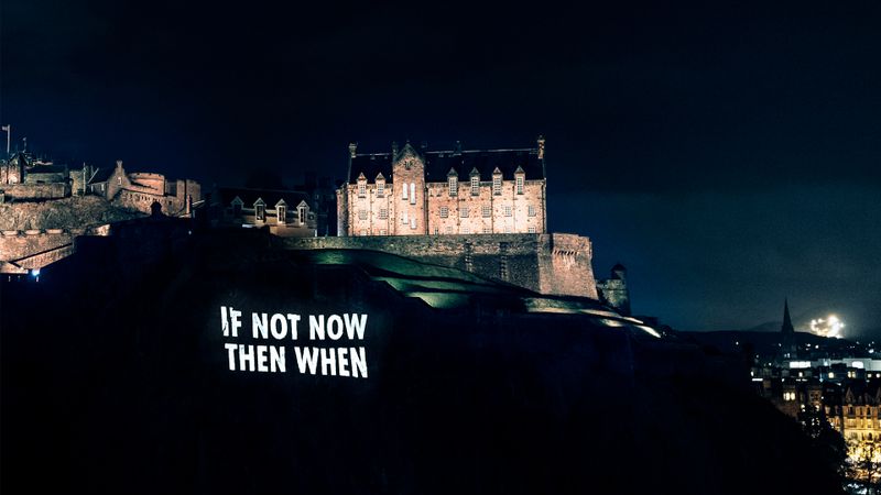 "If not now then when" projected onto the cliff face below Edinburgh Castle in block capitals