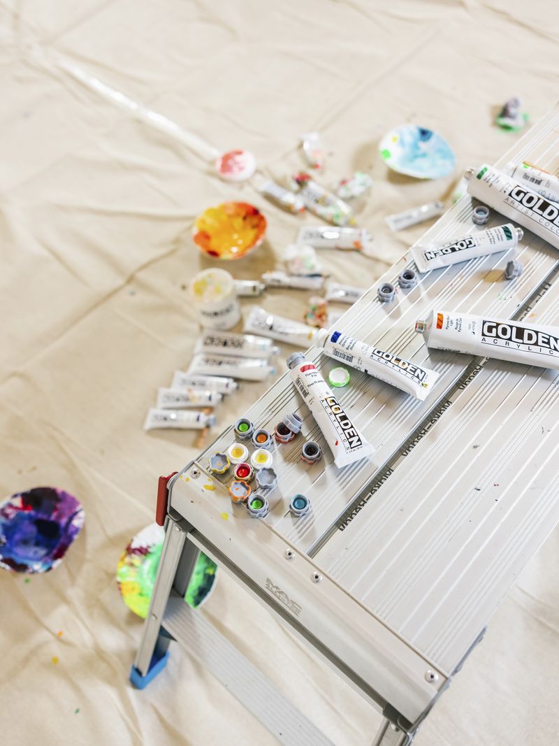 open and half-used tubes of acrylic paint on a metal bench and on the floor