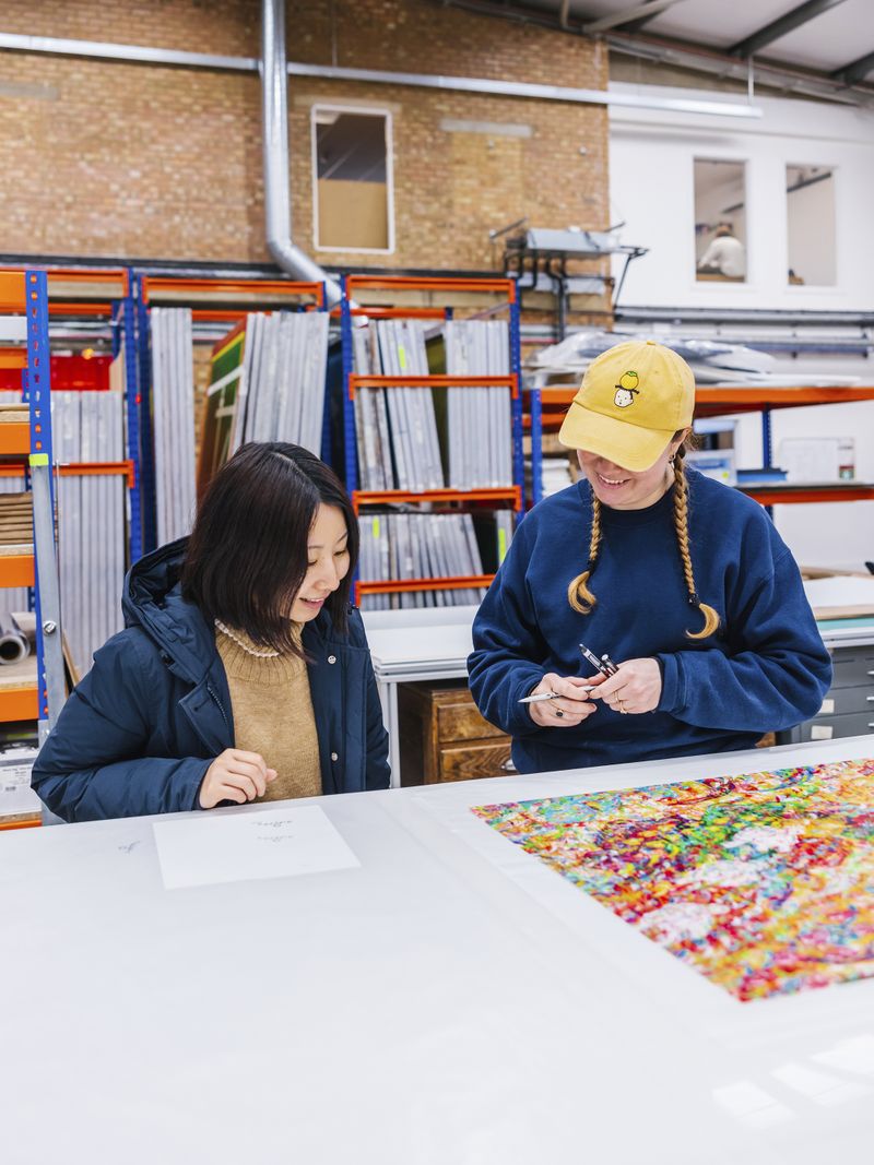 Ayako Rokkaku discussing the proof for her print edition with a printmaker wearing a yellow cap