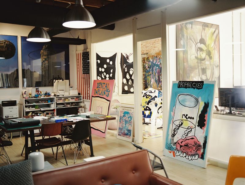 Interior of a Darren Romanalli studio showing desk and multiple artworks hanging and standing against the wall