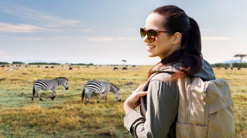Turistka s batohem pozoruje v savaně zebry