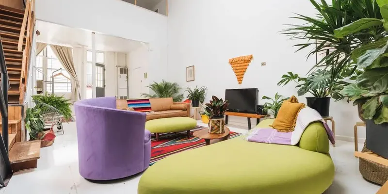 Loft in NYC with green and purple couches, tv, green plants and white walls and floor