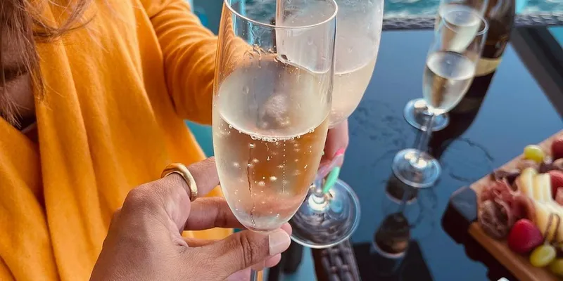 Two people toasting two glasses of bubbly drink on Miami terrace with ocean in the background
