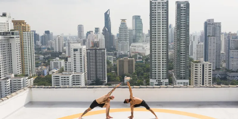 Two people doing yoga Triangle Pose on helicopter pad overlooking skyscrapers