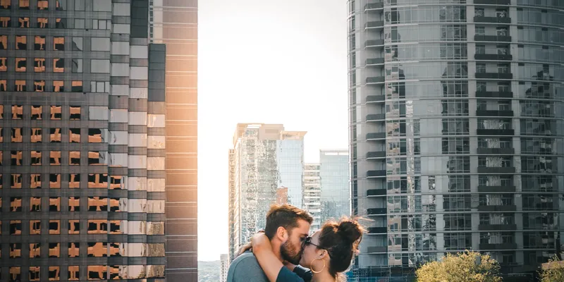 Two people kissing on an outdoor platform surrounded by skyscrapers