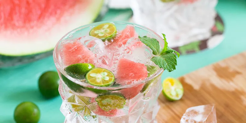 Glass of mojito with lime, watermelon and ice on wooden plank