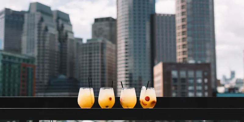 4 glasses with orange liquid on ledge with skyline background