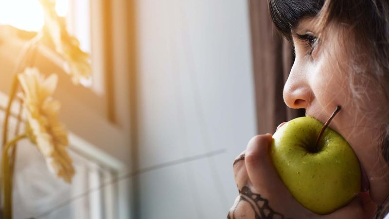 Girl eating an apple while looking out of the window