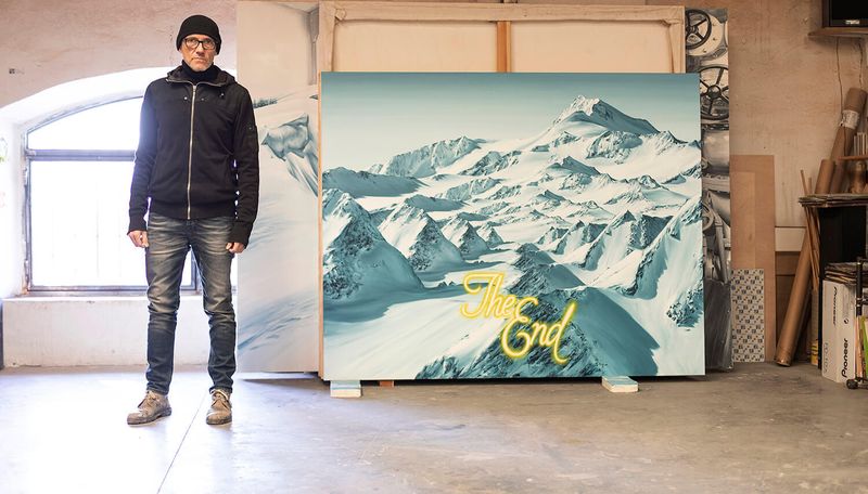 Paco Pomet stood in his studio alongside a painting of mountains with several canvases stacked up behind it