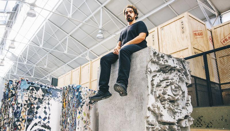 Vhils sat on a stone block with an eye carved into it amongst storage boxes in his studio