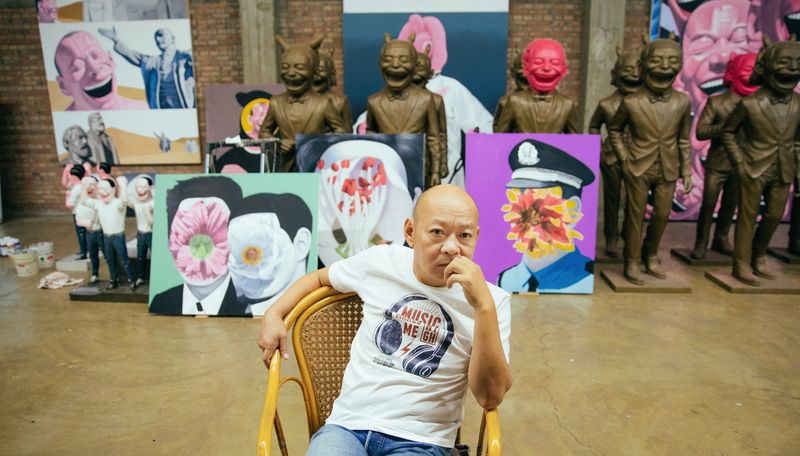 Yue Minjun holding a hand up to his face whilst sitting in his studio
