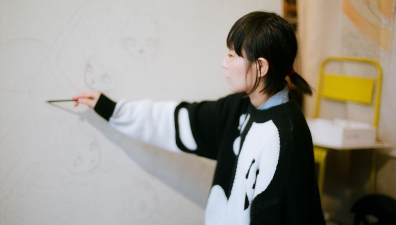 Aya Takano reaching forwards to raise a pencil to a canvas
