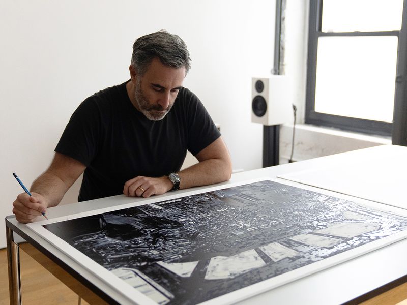 artist sitting behind table, signing a large monochromatic screenprint