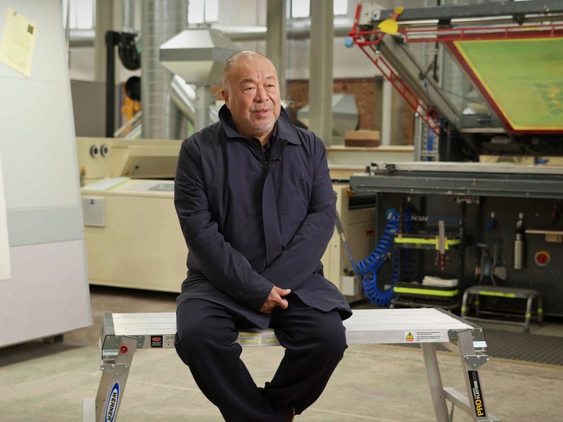 Ai Weiwei sitting on a metal bench in a print studio