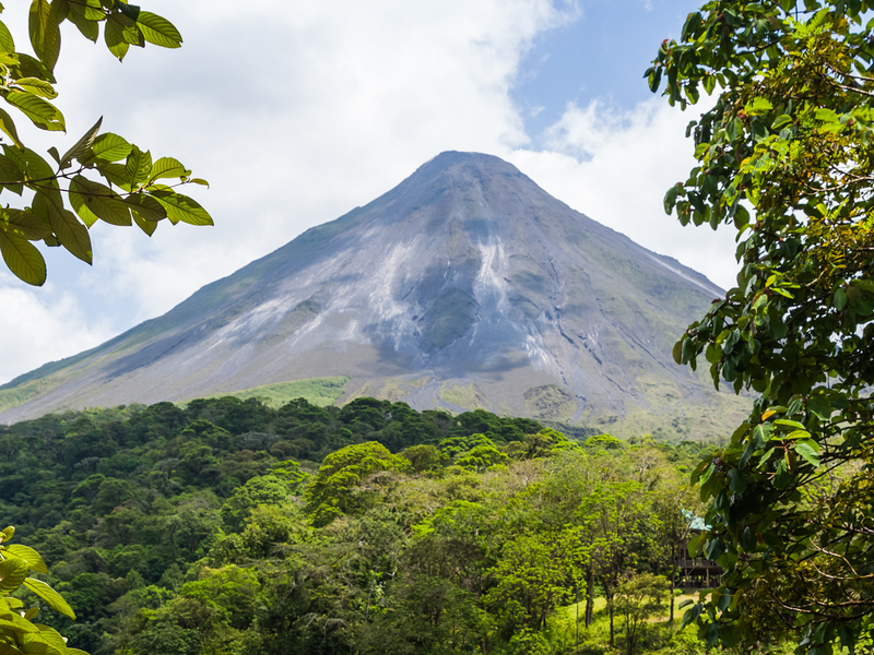 view of arenal volcano through lush rainforest trees in costa rica