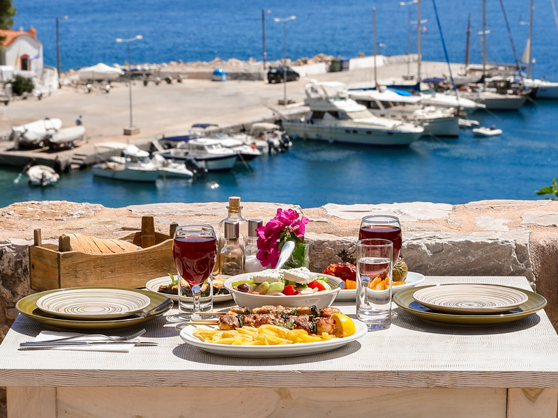 table set for a traditional greek meal overlooking a harbor with boats