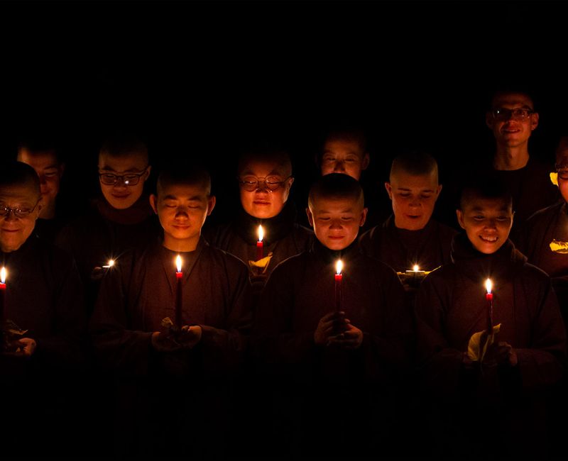 En grupp nunnor och munkar upplysta av ljus som de håller mellan sina händer. De är en kör som sjunger. 