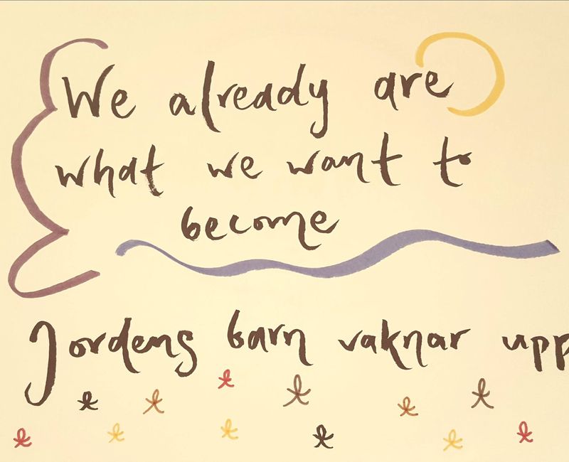 En tuschteckning med texten: We already are what we want to become. Jordens barn vaknar upp. Under texten finns enkla streckfigurer