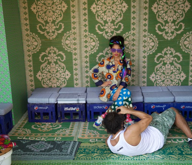 artist on floor getting a lower angle taking a photograph of model seated against green patterned wallpaper