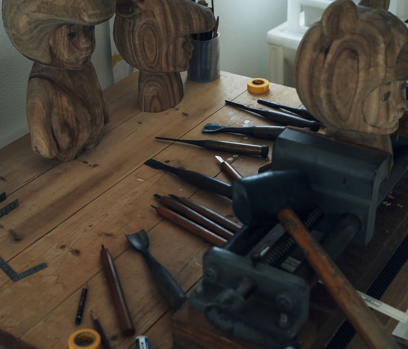 a table in the artist's studio with wooden carved figures on it and a selection of tools