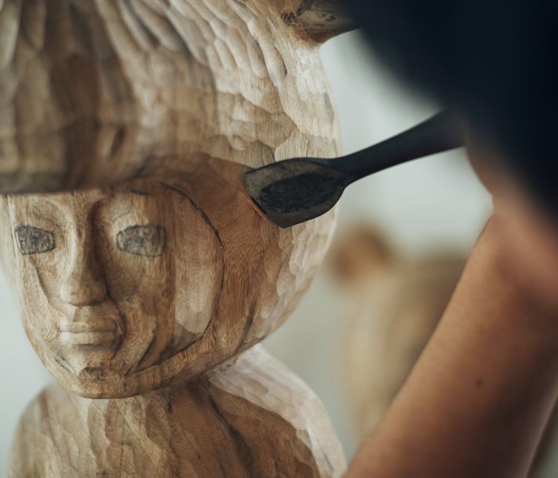 close-up of the head of a wooden sculpture with the artist working into it with a carving tool 