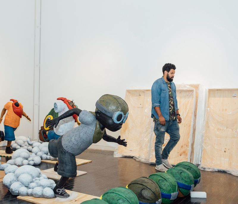 Hebru Brantley walking through large studio space surrounded by three large sculptures of his